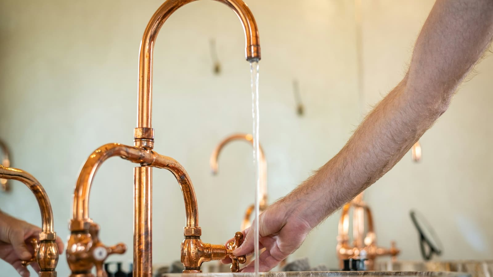 Hand reaching toward running water from polished copper faucets over a stone basin